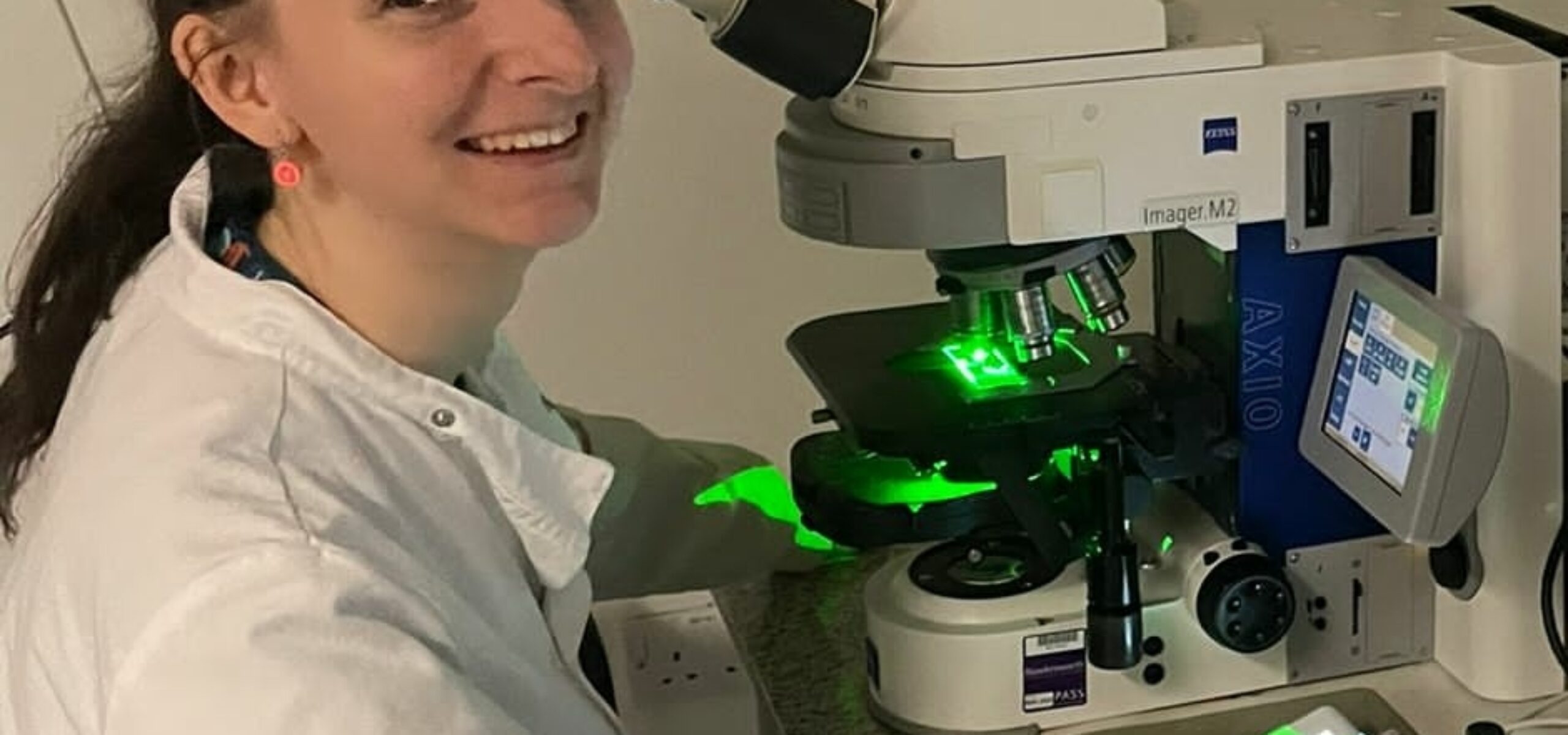 Charlotte Mellor looking at the camera, with a microscope and computer screen in the background.