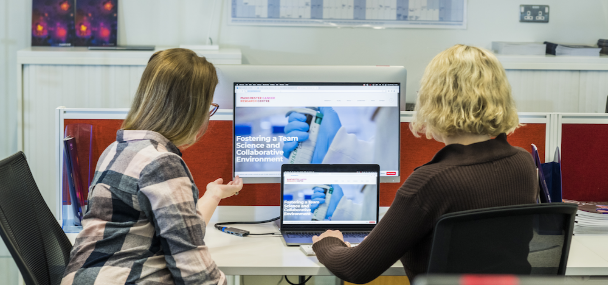 Two people looking at a computer screen and a laptop