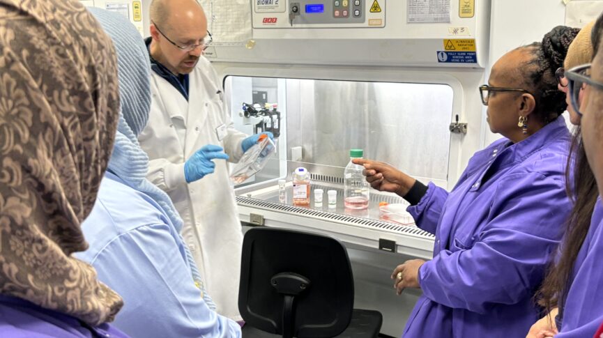 A man in a white lab coat showing cells to people in purple lab coats in a laboratory 